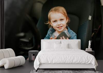 Little girl in a car seat. Holding phone in her hand. Taking driver seat. Car damage. Authentic image Wall mural