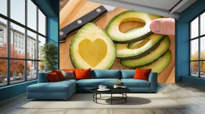 Male Hand Prepares Fresh Cut Avocado With Heart Shaped Pit Area On Wooden Cutting Board Wall mural