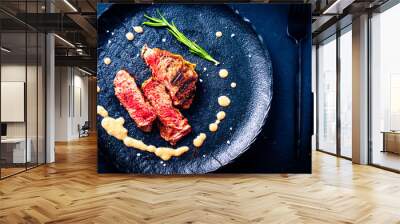 Lightly fried marbled beef rar steak cut into pieces with rosemary and sauce on a black plate Wall mural