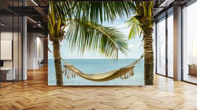 A hammock strung between two palm trees, gently swaying with the ocean in the background Wall mural