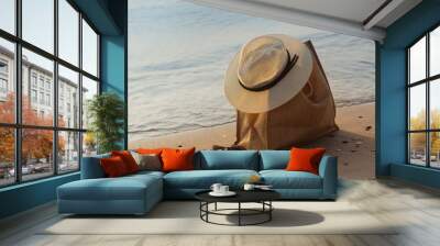 a female summer hat rests on a bag on the seashore, on the sand, early morning, the concept Wall mural