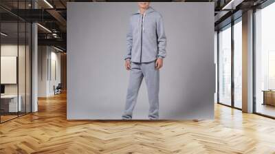 A teenager with a gray tracksuit, on a gray background, stands in full growth and smiles Wall mural