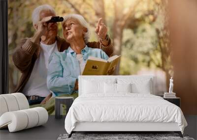 Happy senior couple bird watching in park for relax bonding time together, freedom and retirement peace on outdoor bench. Elderly marriage love, binoculars and book reading woman with man pointing Wall mural