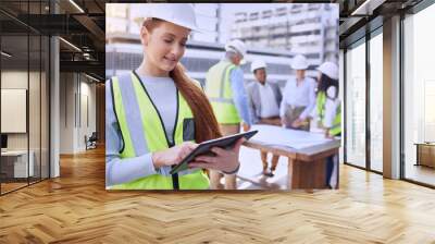 Construction is underway. an attractive young female construction worker using a tablet while standing outside with her team in the background. Wall mural