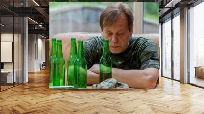 Elderly man in military uniform drinking beer, lots of empty bottles, neutral background. Concept: war veteran, family problems, post-traumatic syndrome, alcoholism, beer addiction. Wall mural