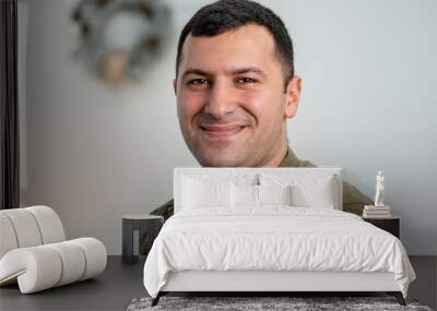 Portrait of a smiling man of oriental appearance against the background of a shelf with books and a table lamp, light tone. Wall mural