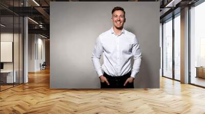 Handsome young man posing on grey background in white dress shirt while smiling Wall mural