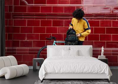 Millennial holding his bagpack in urban area next to his fixed gear bike. Wall mural