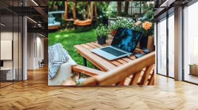 A person works on a laptop at a wooden table in a vibrant garden filled with blooming flowers. The sun shines on a peaceful, inviting space perfect for relaxation and productivity Wall mural