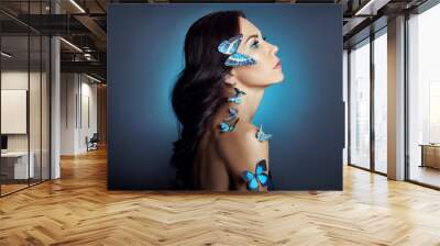 Beautiful mysterious woman with butterflies blue color on her face, brunette and paper artificial blue butterflies on the girls body. Bright green eyes, long black curly hair Wall mural