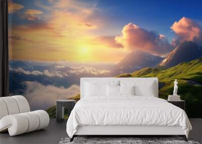 The sun rises over lush green hills, casting a warm glow on the landscape, while clouds drift lazily between towering mountains in the distance Wall mural