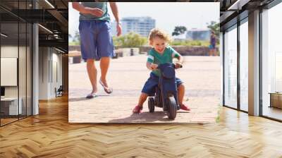 Happy, toy and motorbike with child and father playing in park for bonding, laugh and fun. Smile, happiness and energy with man and young boy riding on scooter for playful, youth and summer Wall mural