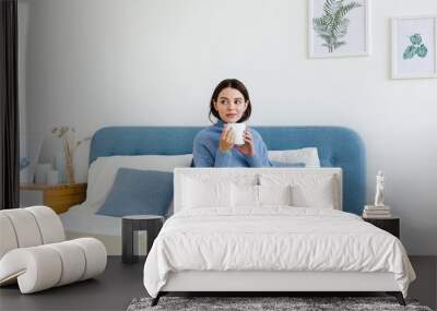 Girl in a blue sweater in interior Hygge style with a cup in hand sits on the bed Wall mural