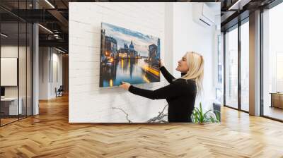 Attractive happy young woman wearing holding photo canvas in her hands. Wall mural