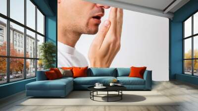 Bad breath. Halitosis concept. Young man checking his breath with his hand. Wall mural