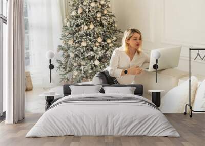 Beautiful girl in a room with a Christmas tree enjoys a laptop Wall mural