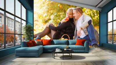 Couple in love sitting on autumn fallen leaves in a park, enjoying a beautiful autumn day. Man kissing a woman in a forehead Wall mural