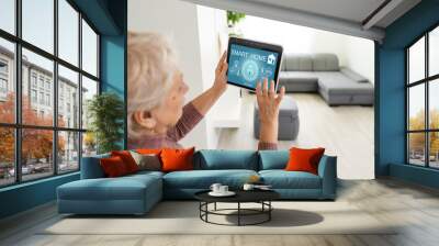 Senior woman at home standing at kitchen holding digital tablet controlling smart home system back view checking cameras close-up Wall mural