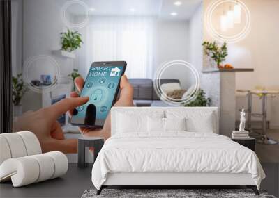 Smart home technology interface on smartphone app screen with augmented reality (AR) view of internet of things (IOT) connected objects in the apartment interior, person holding device Wall mural