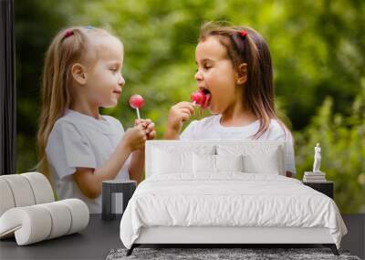 Two cute little sisters eating huge lollipops outdoors on beautiful summer day Wall mural