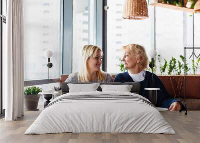 Two happy women talking in cafe. Aged woman and her adult daughter drinking coffee at cafe. Mothers day. Wall mural