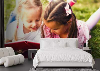 Two young girls lying on the grass outdoors reading separate books. These siblings are enjoying time together as family during summer Wall mural