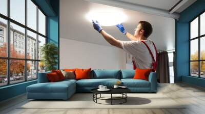 Worker installing lamp on stretch ceiling indoors. Wall mural