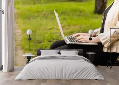 Young attractive businesswoman using a pc laptop computer while sitting on a wooden bench in a city park. Wall mural