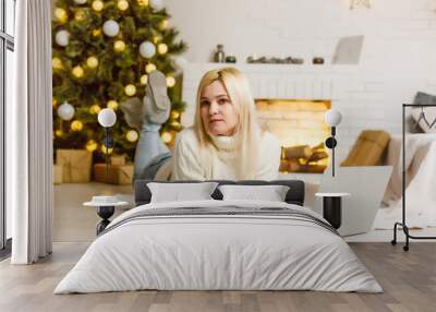 Young woman relaxing with her laptop in front of a Xmas tree lying barefoot on the floor surrounded by Christmas gifts Wall mural