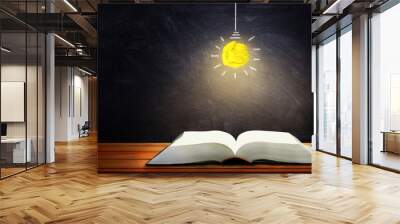 Business Idea, Education and Learning Concept : Yellow crumpled paper light bulb light glowing on opened book with chalkboard in background. Wall mural