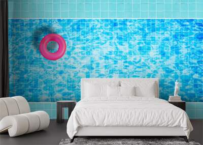 Pink inflatable floating ring floating on blue water in swimming pool surrounded with tiles mosaic floor from top view. Wall mural