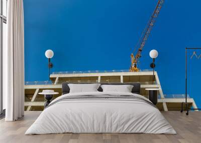 Tower crane and unfinished building an apartment house on a background of blue sky Wall mural