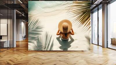 Aerial view of girl sitting with hat on a white sandy coast, blue ocean and shadows from palm leaves. Generative AI Wall mural