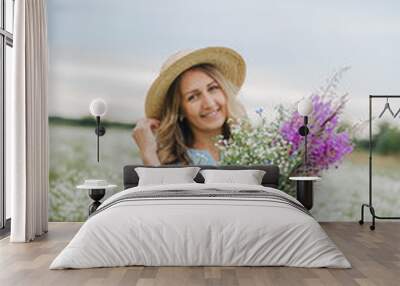 beautiful blonde girl in a field of daisies. woman in a blue dress in a field of white flowers. girl with a bouquet of daisies. summer tender photo in the village. wildflowers. girl in a straw hat Wall mural