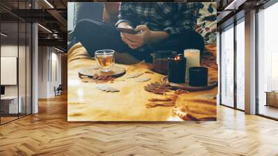 Young woman using smart phone while sitting on bed relaxing at home, drink tea in autumn fall season. Concept of cozy autumn at home, hygge Wall mural