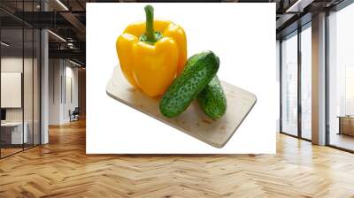 Yellow bell pepper and 2 small cucumbers on wooden cutting board isolated on white background Wall mural