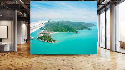 Aerial view of airplane flying above   clouds and sky. Airplane wing fly over tropical green island. View from the plane window. Wall mural