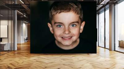 Beautiful portrait of a happy smiling boy with beautiful blue eyes and a beautiful smile. Baby face on black background Wall mural