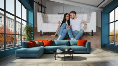 Young happy couple sitting on the floor at home and looking on each other  Wall mural