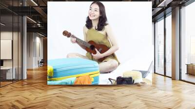 Asian woman playing guitar while preparing clothes for summer trip Wall mural