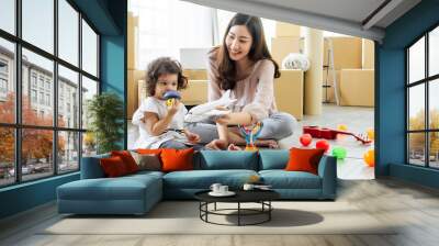 Beautiful adult Asian woman or mother and little cute daughter moving new house, home or apartment, playing bubble together on the floor in comfortable living room with many paper unpacking boxes. Wall mural