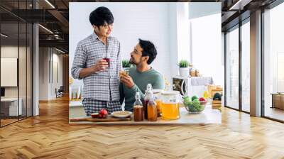 Handsome man smiling with happiness, serving boyfriend glass of Kombucha healthy fermented probiotic tea drinks with ingredients red apples, strawberries, mushroom scoby at home. LGBT gay Concept. Wall mural