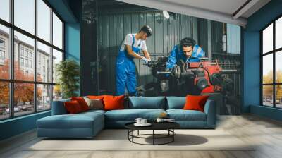 Two adult handsome male mechanics wearing uniform, using machine for fix, repair car or automobile components, teamwork helping, working in car maintenance service center or shop. Industry Concept. Wall mural