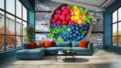   A bowl filled with red and blue berries sits on a wooden table beside a lush green plant Wall mural