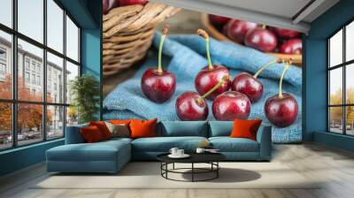   A cluster of cherries resting atop a blue fabric surface alongside a wooden table's basket containing cherries Wall mural