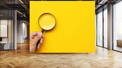  a person's hand holding a magnifying glass over a yellow background with a hand holding a magnifying glass. Wall mural