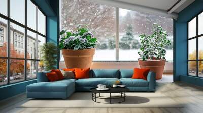   Two potted plants rest on a window sill, framing the snow-covered window and winter landscape beyond Wall mural