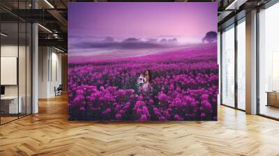 A beautiful girl in a pink dress standing with a lantern full of magic lights in a large pink field of willow herb. Romantic evening photo with sunset sky.
 Wall mural