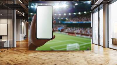 A hand holding a smartphone with a white mockup screen at a sports stadium Wall mural