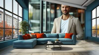 A joyful man in a casual business attire is using a tablet in a bright, modern office environment. Wall mural